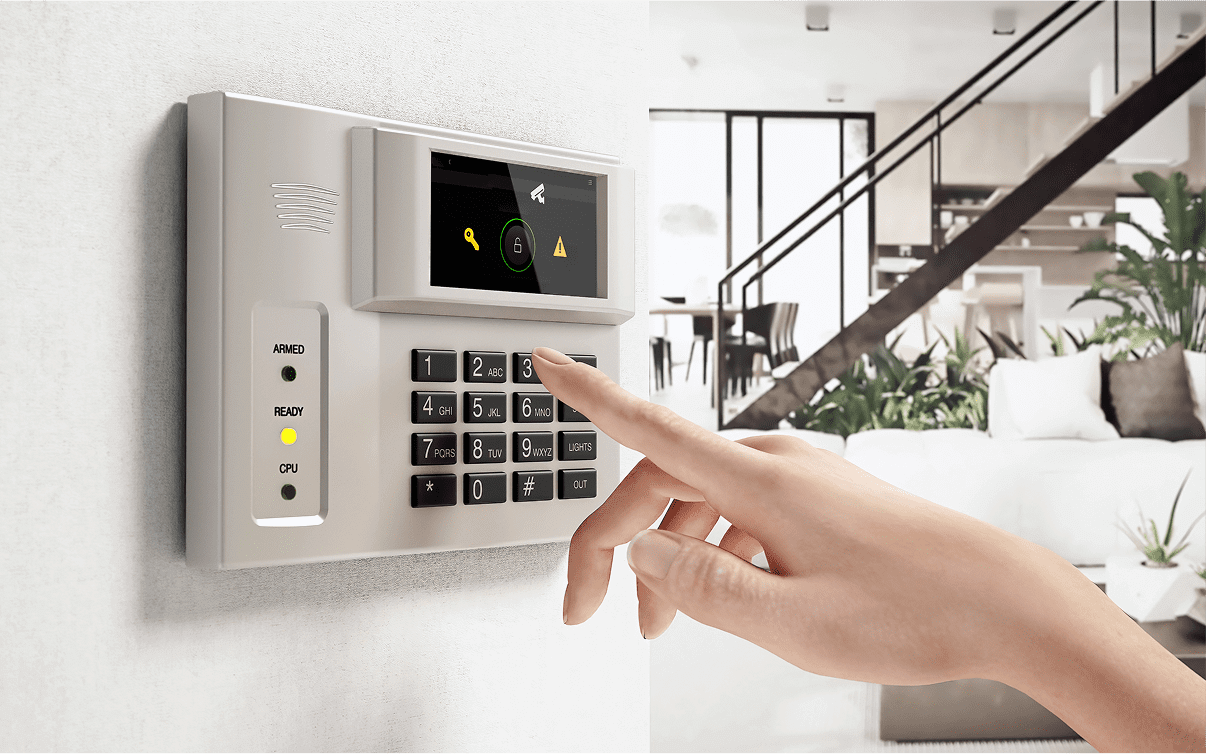 A hand pressing buttons on a wall-mounted security keypad located in a modern, spacious living room.